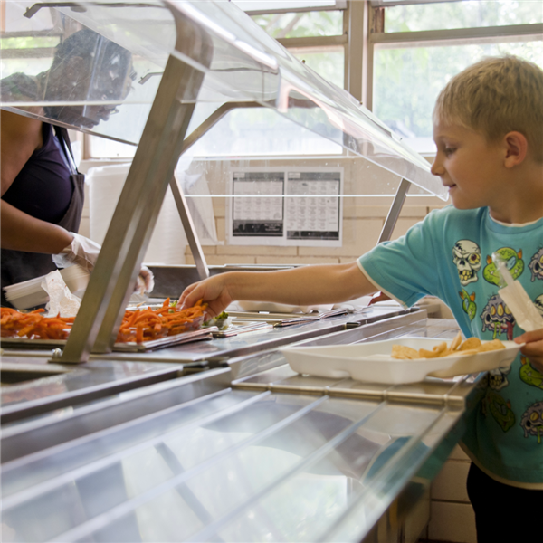  A young boy reaches for a serving of food from a cafeteria line.